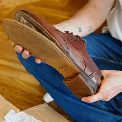 Une personne examine une chaussure en cuir marron, montrant l'usure de la semelle.