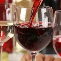 Czerwone wino nalewane do kieliszka, obok białe wino i butelki. Zastanawiasz się, ile kalorii ma wino?