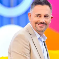 Krzysztof Ibisz, znany z programów telewizyjnych, uśmiecha się w beżowej marynarce. Jego wiek dodaje mu charyzmy.