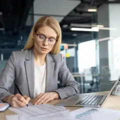 Kobieta w okularach analizuje dokumenty, pracując przy biurku. Dbałość o szczegóły to klucz do przestrzegania praw pracodawcy.