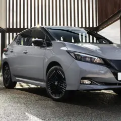 Szary Nissan Leaf stoi przed nowoczesnym budynkiem z przeszklonymi ścianami.