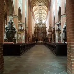 Wnętrze katedry w Pelplinie z rzędami ławek i bogato zdobionym ołtarzem głównym.