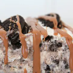 En bit krämig oreo cheesecake med chokladsås som rinner ner.