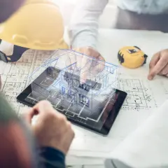 Architekci analizują projekt domu 3D na tablecie, plany i żółty kask.