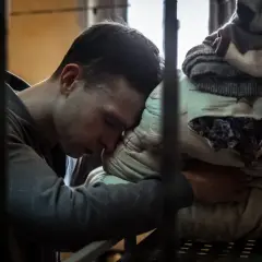 Młody mężczyzna opiera głowę na poduszce w celi. Scena z filmu o Tomaszu Komendzie, ukazująca jego trudne chwile.