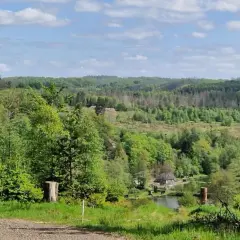 Grüne Hügel und Wälder säumen die Eckenhagen Route. Ein kleiner Teich mit einem Haus liegt eingebettet in der Landschaft.