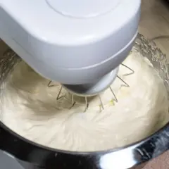 Mieszadło robota kuchennego ubija puszysty krem z ricotty do ciasta.