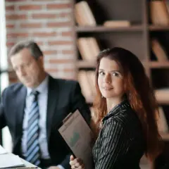 Kobieta z dokumentami w ręku i mężczyzna w garniturze przy biurku. Zastanawiają się, ile trwa uzasadnienie wyroku.