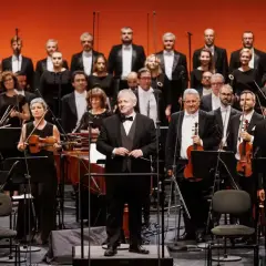 Orkiestra i chór przygotowują się do wykonania **Moniuszko opery**. Dyrygent stoi na podwyższeniu, gotowy do rozpoczęcia.