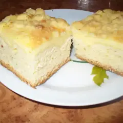Dwa kawałki puszystego ciasta drożdżowego z serem i kruszonką, podane na białym talerzu.