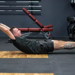 Mężczyzna wykonuje ćwiczenie hollow body hold na siłowni, napinając mięśnie brzucha.