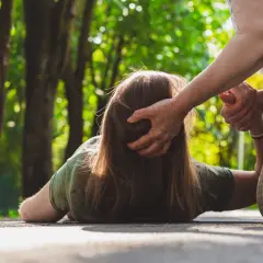 Osoba na ziemi, być może doświadczająca nietypowych objawów padaczki, otrzymuje pomoc od drugiej osoby.