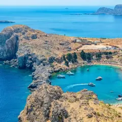 Malownicza zatoka na Rodos, idealna do zwiedzania samochodem. Woda krystalicznie czysta, plaża pełna ludzi, a wokół skaliste wybrzeże.