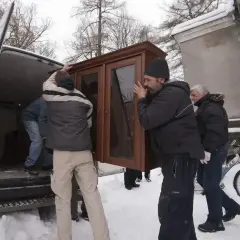 Mężczyźni wynoszą mebel z domu, przygotowując się do przeprowadzki. Widać śnieg i zimową aurę, co może sugerować trudności związane z eksmisją w okresie ochronnym.