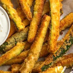 Bastoncini croccanti di zucchine in friggitrice ad aria, dorati e invitanti, serviti con una salsa cremosa.