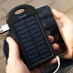 Ręce trzymające powerbank na rower z panelem słonecznym ładujący telefon. Idealny na wycieczki!