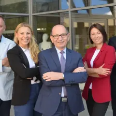 Profesor nadzwyczajny w okularach i jego zespół pozują do zdjęcia przed budynkiem.