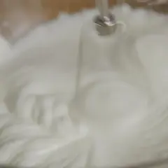 Un batteur électrique fouette un œuf blanc en neige dans un bol en verre, créant une texture aérienne et mousseuse.