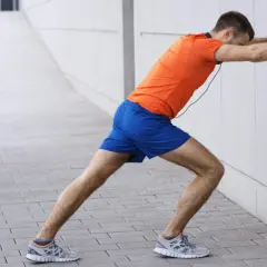 Un homme en tenue de sport fait un étirement mollet contre un mur blanc.