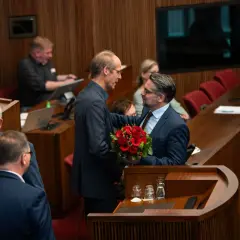 Ein Mann überreicht Mark Rackles einen Blumenstrauß in einem Sitzungssaal.