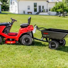 Czerwony traktorek ogrodowy z czarną przyczepką do traktorka na zielonej trawie, gotowy do pracy.