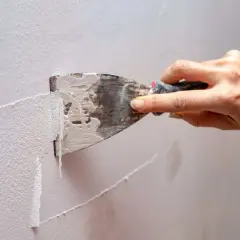 Mano usa una spatola per rimuovere la pittura lavabile dal muro, un passo fondamentale per preparare la parete a una nuova tinteggiatura.
