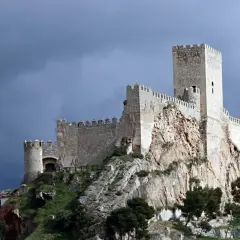 Castillo medieval en lo alto de un peñasco, parte de la ruta de la lana, bajo un cielo tormentoso.