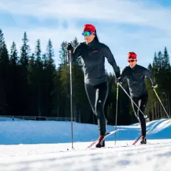 Dwie kobiety w sportowych strojach pokonują trasę narciarską. Długość nart biegowych jest kluczowa dla ich szybkości i stabilności na śniegu.