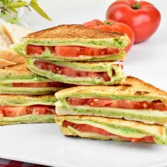 Pyszne włoskie kanapki z serem, pomidorami i zielonym pesto, ułożone na talerzu.