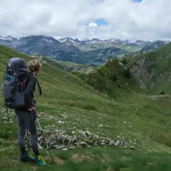 Une randonneuse admire le panorama des Pyrénées, prête pour son trek. Le soleil perce les nuages sur les sommets enneigés.