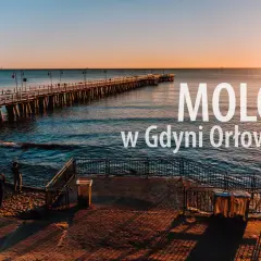 Zachód słońca nad morzem w dzielnicy Gdyni z molo. Długie molo w Orłowie, spokojne fale i dwie osoby na plaży.