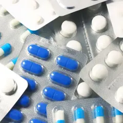 Blistry z białymi i niebiesko-białymi kapsułkami oraz okrągłymi białymi tabletkami, jak polopiryna.