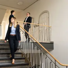 Zwei Frauen und zwei Männer in Business-Kleidung gehen eine Treppe hinunter. Sie könnten sich auf dem Weg zu einem LLM-Kurs berufsbegleitend befinden.