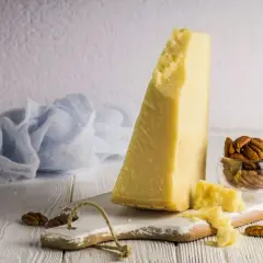 Kawałek sera Grana Padano, czy to parmezan? Obok orzechy pekan i błękitna tkanina.