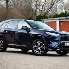 Ciemnoniebieski Toyota RAV4 Hybrid zaparkowany przed garażami.