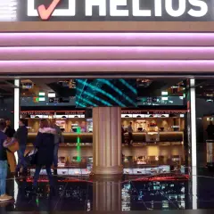 Ludzie wchodzą do kina Helios. Zastanawiasz się, ile kosztuje średni popcorn w Heliosie? Warto sprawdzić ceny przy barze.