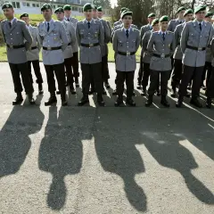 Soldaten der Bundeswehr in Uniform mit grünen Baretts stehen Spalier. Ihre Schatten werfen lange Linien auf den Asphalt.