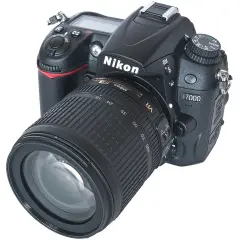 Nikon D7000 z obiektywem 18-105mm VR. Aparat cyfrowy z widocznymi przyciskami i pokrętłem trybów. Dane techniczne tego modelu są imponujące.