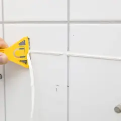 Main jaune en action pour enlever silicone vinaigre. Le joint est retiré proprement.