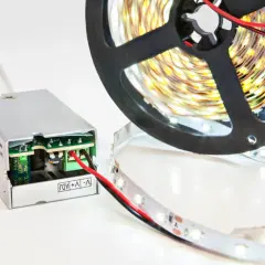 Podłączenie zasilacza LED do taśmy świetlnej. Metalowa obudowa zasilacza z widoczną płytką drukowaną i zielonymi złączami. Obok nawinięta na szpulę taśma LED.