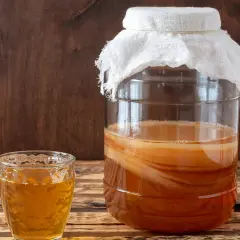 Szklanka z napojem i duży słój z warstwową kulturą SCOBY – tak wygląda domowa kombucha.