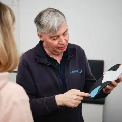 Ein Mann erklärt einer Frau, wie oft man Einlagen verschrieben bekommt, und hält eine orthopädische Einlage in der Hand.