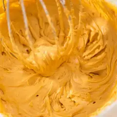 Krem z masy kajmakowej i mascarpone w trakcie ubijania. Widoczne końcówki miksera tworzą faliste wzory w gęstej, złocistej masie.