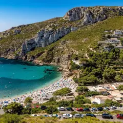 Bahía con aguas turquesas y playa abarrotada, rodeada de acantilados y vegetación. Un paraíso entre las mejores playas de Alicante.