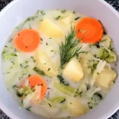 Miseczka zupy z młodego kapusty z ziemniakami i marchewką, ozdobiona koperkiem.
