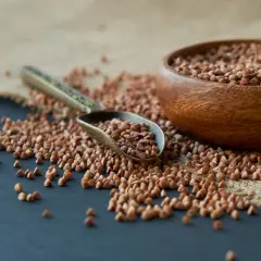 Łyżka z kaszą gryczaną obok drewnianej miski. Czy pies może jeść kaszę gryczaną? Tak, jest zdrowa dla psów.