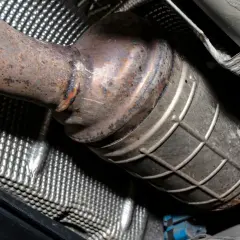 Podwozie samochodu z widocznym, zardzewiałym elementem układu wydechowego. Czy diesel ma katalizator? Tak, ten element to właśnie katalizator.