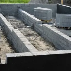 Budowa fundamentów: jak połączyć stary fundament z nowym. Ściany z bloczków betonowych, materiały budowlane na paletach.