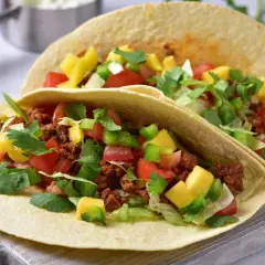 Dwa tacos z mielonym mięsem, pomidorami, papryką, mango i kolendrą na desce.