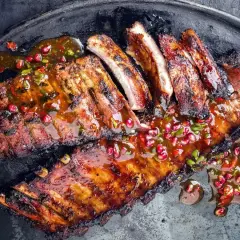 Soczyste żeberka w marynacie, polane aromatycznym sosem z granatem i chili, podane na metalowej tacy.